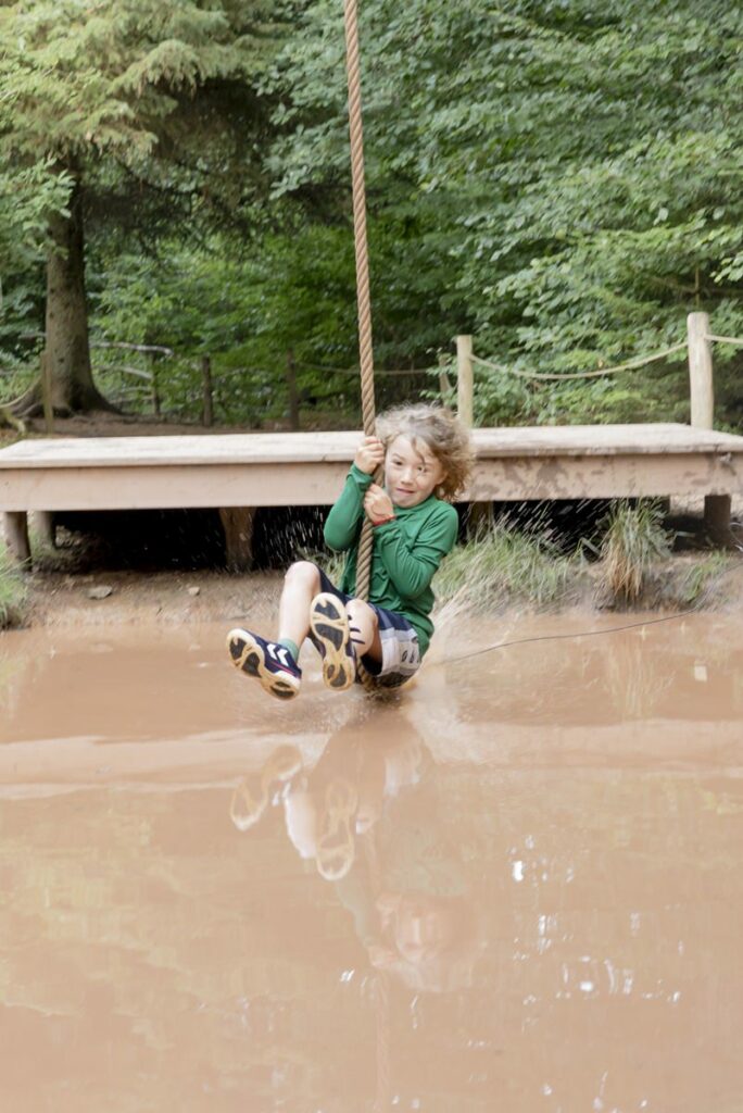 ein Junge schwingt an einem Seil über ein Wasserhindernis im Arboretum Naturparcours | Foto: Hanna Witte