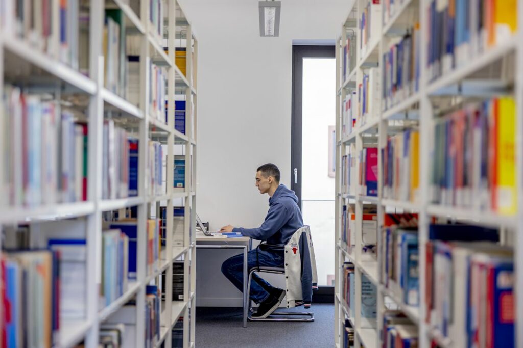 ein Student der Uni Siegen sitzt in der Bibliothek und arbeitet an seinem Laptop | Foto: Hanna Witte
