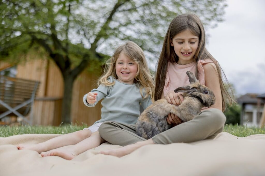 zwei Mädchen sitzen auf einer Picknick-Decke und streicheln ein Kaninchen von Hof Hardthöhe | Foto: Hanna Witte