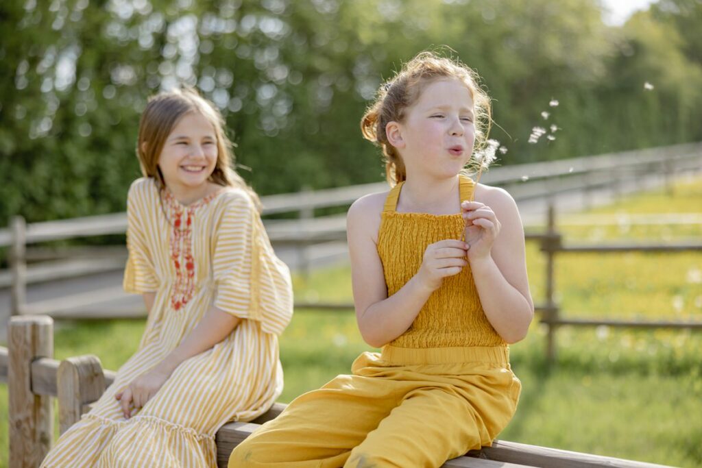 zwei Mädchen sitzen gemeinsam auf einem Zaun von Hof Hardthöhe und eine pustet eine Pusteblume | Foto: Hanna Witte
